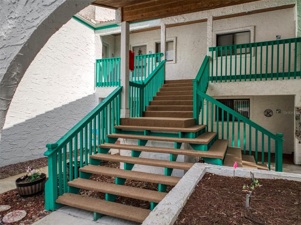 An exterior view of a building with a central staircase featuring green railings and carpeted steps — 4729 CASABLANCA CIRCLE UNIT C22, SEBRING, FL