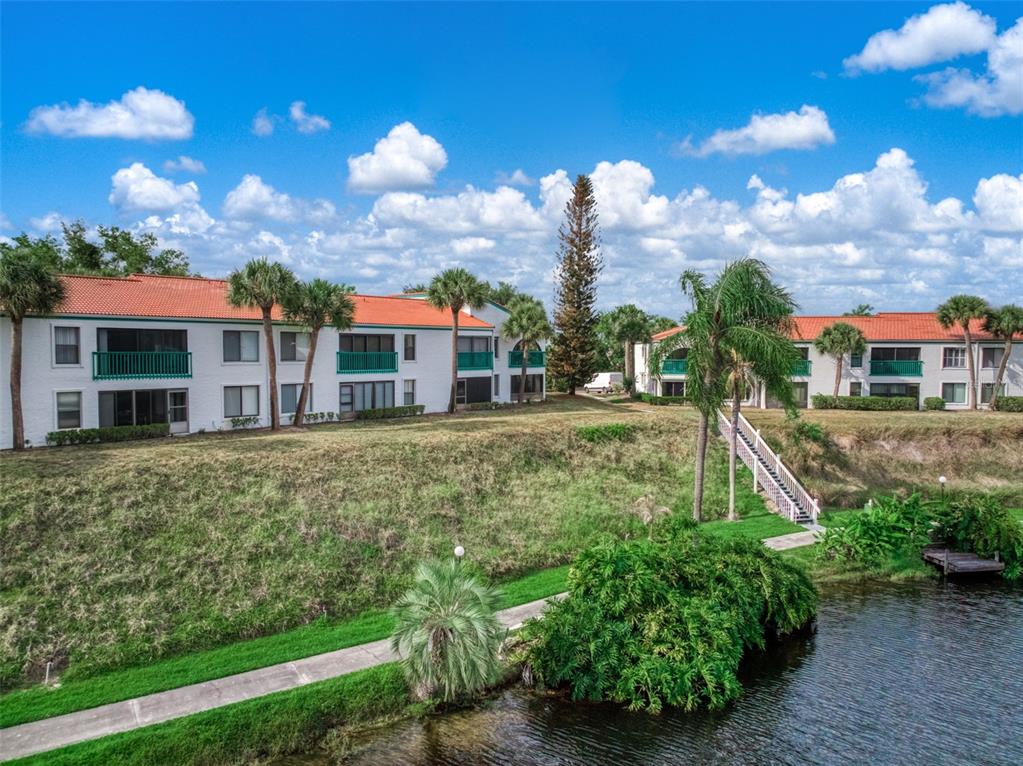Two white apartment buildings with orange roofs sit above a canal with a staircase — 4729 CASABLANCA CIRCLE UNIT C22, SEBRING, FL