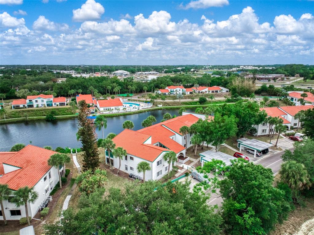 An aerial view shows multiple apartment buildings with orange tile roofs surrounding a central pond — 4729 CASABLANCA CIRCLE UNIT C22, SEBRING, FL