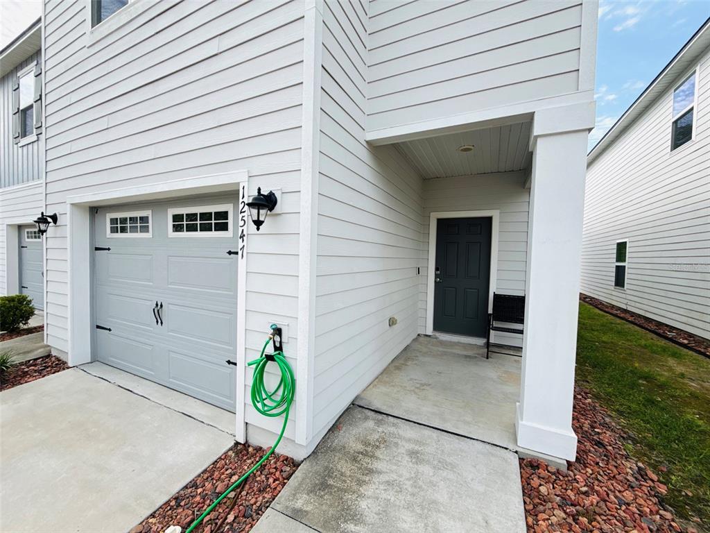 A white house exterior features a gray garage door, a front door, and a green hose — 12547 NW 7TH PLACE, NEWBERRY, FL