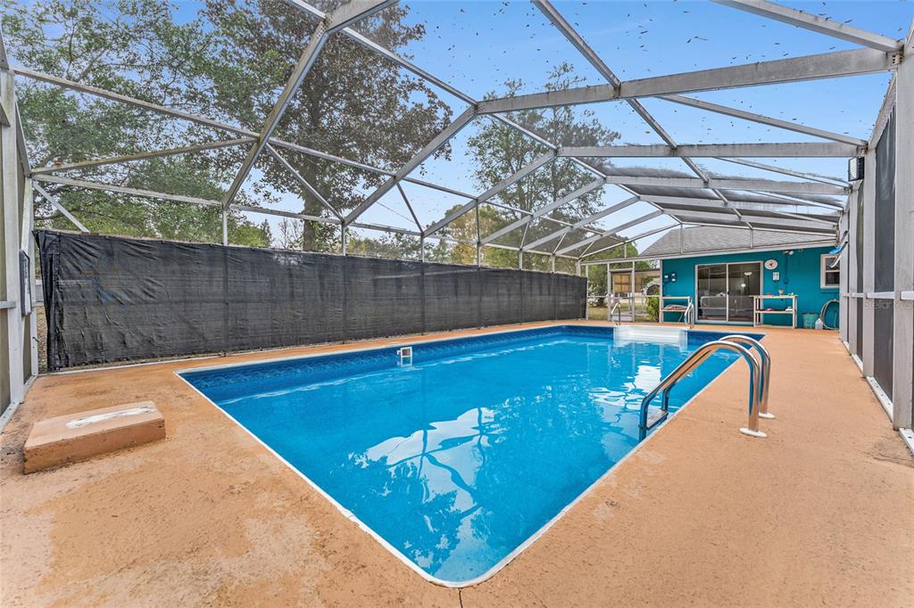 A rectangular swimming pool is enclosed by a screened lanai with a tan concrete deck — 8345 SW 200TH COURT, DUNNELLON, FL