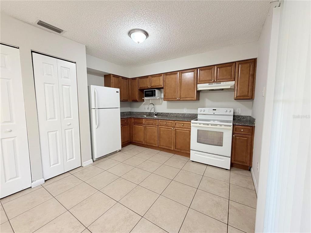 A kitchen features wood cabinets, granite countertops, white appliances, and light-colored floor tiles — 330 DOGWOOD AVENUE, ORANGE CITY, FL