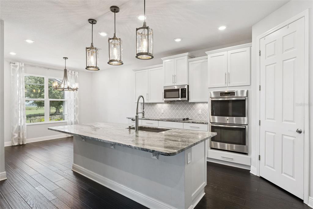A modern kitchen features a large stone island, white cabinetry, stainless steel appliances, and dark flooring — 1511 GATEWAY LANE, KISSIMMEE, FL