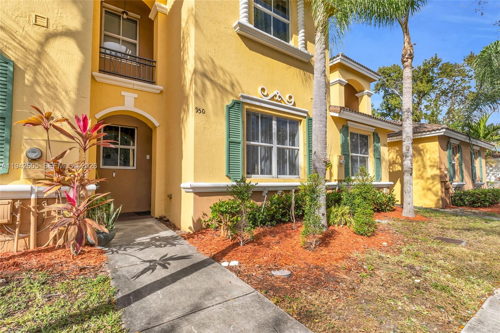 A yellow two-story townhouse features green shutters, a concrete walkway, and a palm tree — 950 NE 42nd Pl, Homestead FL 33033, HOMESTEAD, FL