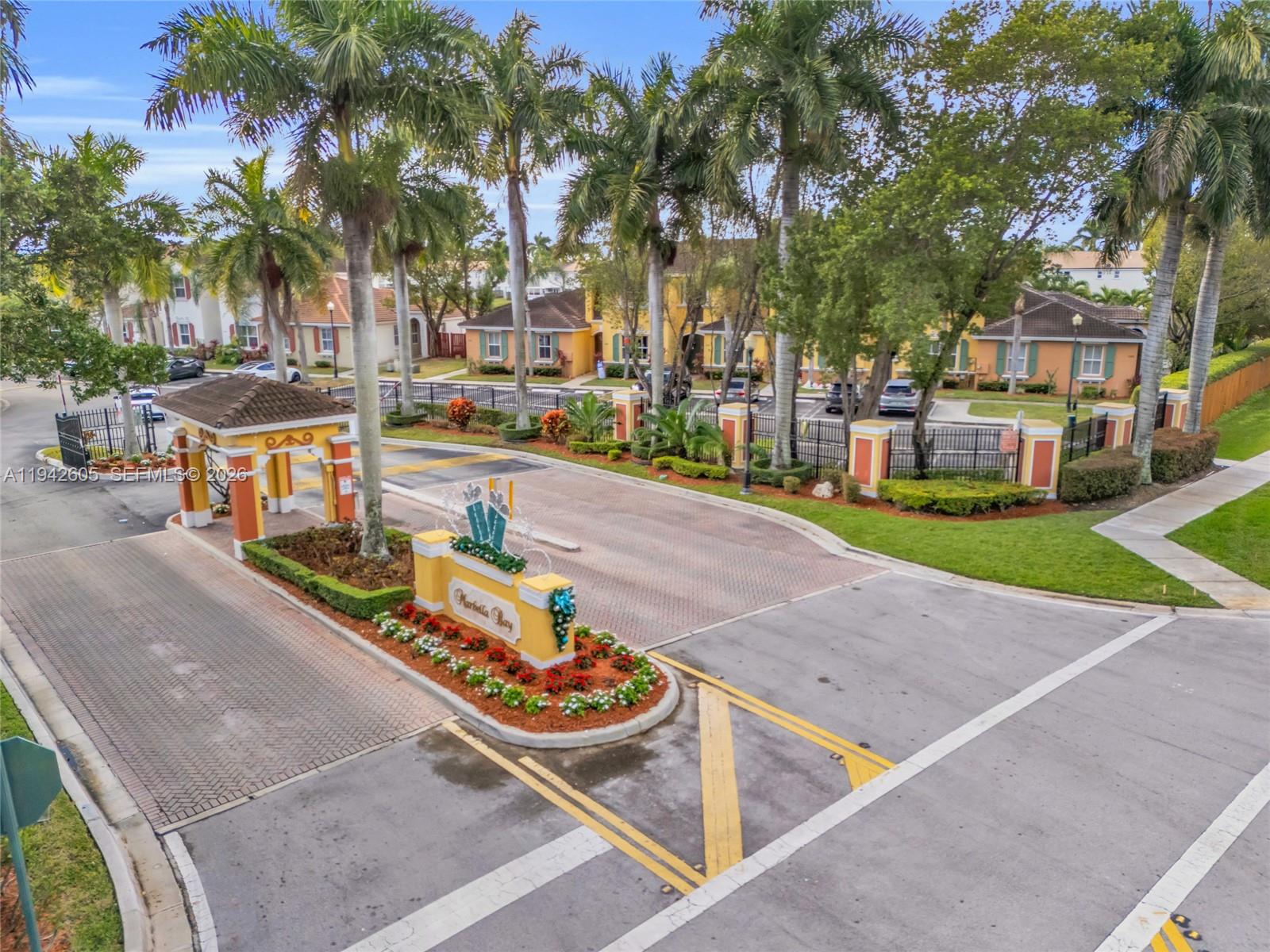 An aerial view of a gated community entrance with palm trees and a landscaped sign — 950 NE 42nd Pl, Homestead FL 33033, HOMESTEAD, FL