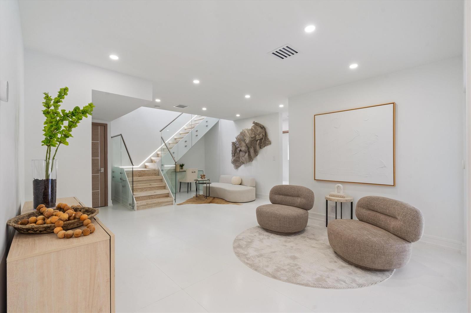 A modern, white-walled living area features a glass-railed staircase, two rounded armchairs, and minimalist decor — 440 NW 11th Avenue, Boca Raton FL 33486, BOCA RATON, FL