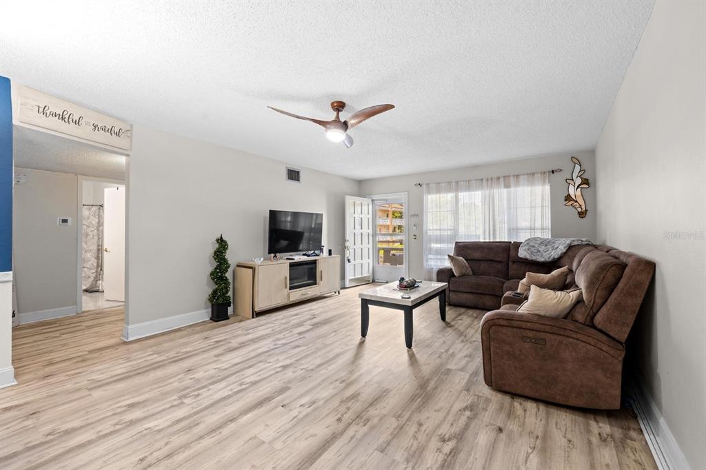A living room features light wood-look flooring, a brown sectional sofa, and a television console — 2416 WORLD PARKWAY BOULEVARD UNIT 26, CLEARWATER, FL
