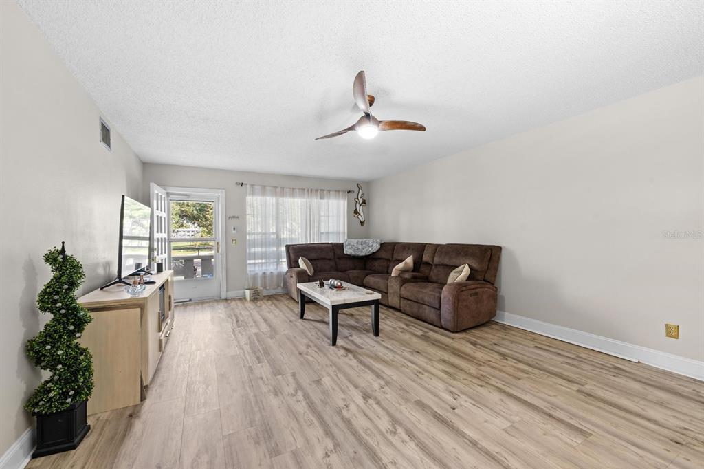 A living room features light wood-look flooring, a brown sectional sofa, and a ceiling fan — 2416 WORLD PARKWAY BOULEVARD UNIT 26, CLEARWATER, FL