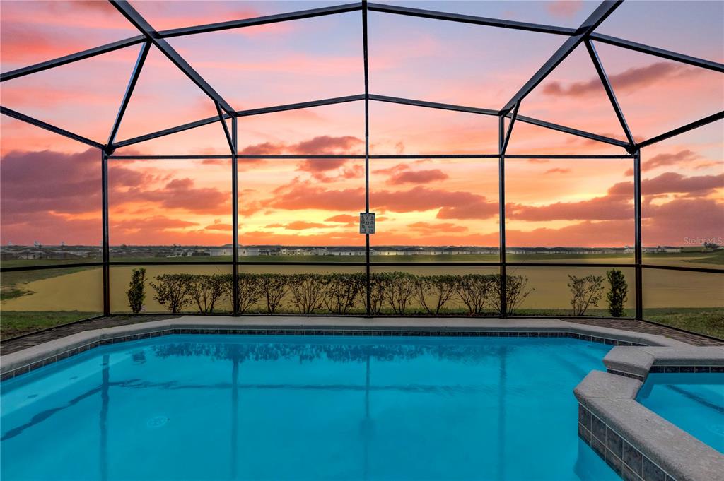 A swimming pool with a spa sits inside a screened enclosure overlooking a sunset view — 1897 SUMMER DRIVE, DAVENPORT, FL