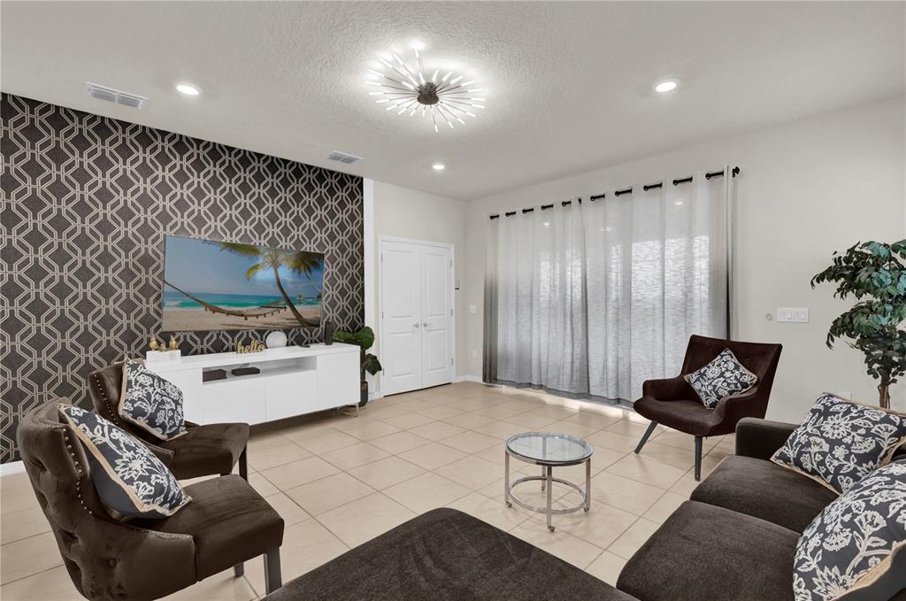 A living room features a patterned accent wall, a white media console, and dark furniture — 1897 SUMMER DRIVE, DAVENPORT, FL