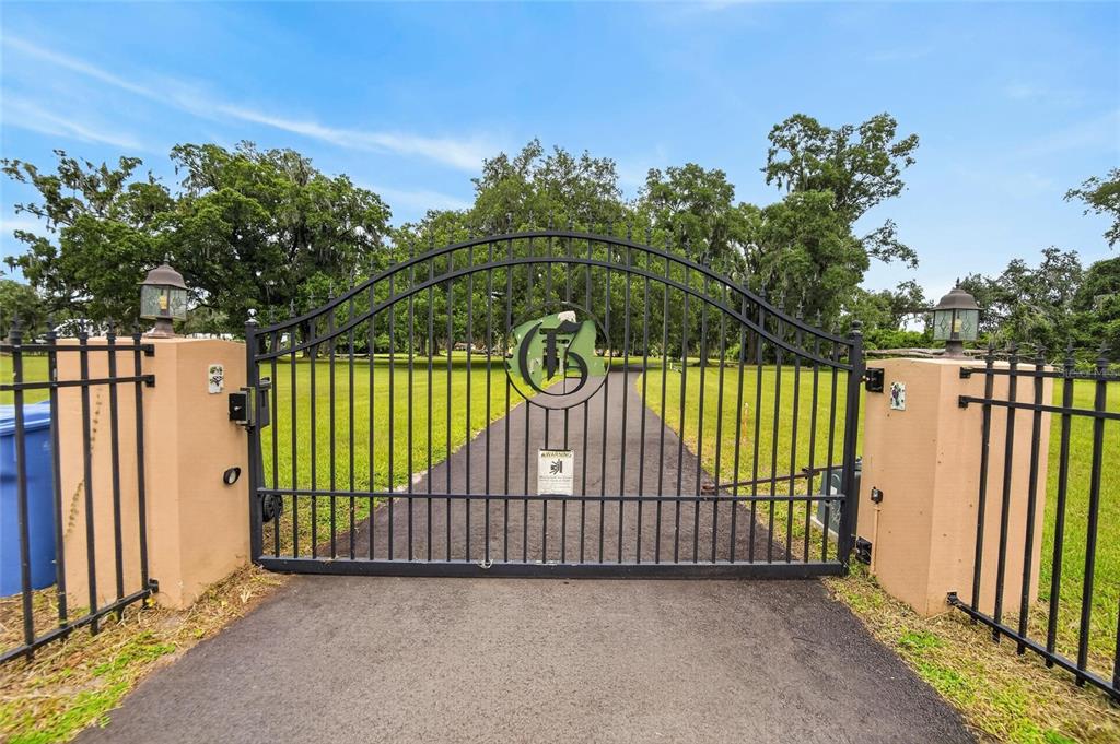A black metal gate with a custom monogram stands between two tan stucco pillars — 4020 N WILDER ROAD, PLANT CITY, FL