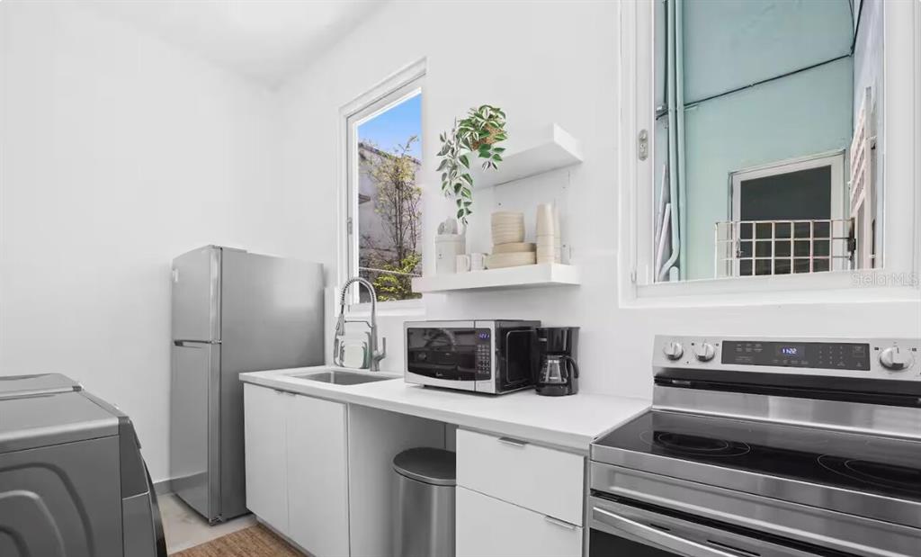 A modern kitchen features white cabinets, stainless steel appliances, and a window overlooking an exterior — 250 CALLE DEL PARQUE UNIT 1A, SAN JUAN, PR