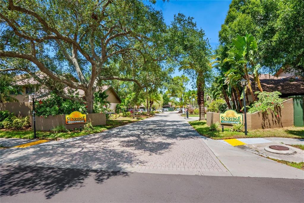 The entrance to Sunridge Condominiums features a paved driveway flanked by two matching stone signs — 956 SUNRIDGE DRIVE UNIT H2, SARASOTA, FL