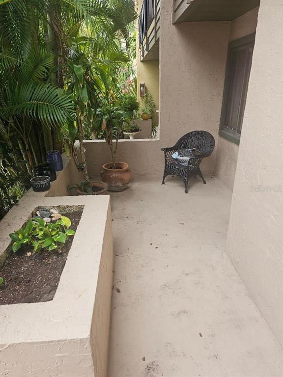 A concrete patio features a built-in planter, potted plants, and a black wicker chair — 956 SUNRIDGE DRIVE UNIT H2, SARASOTA, FL
