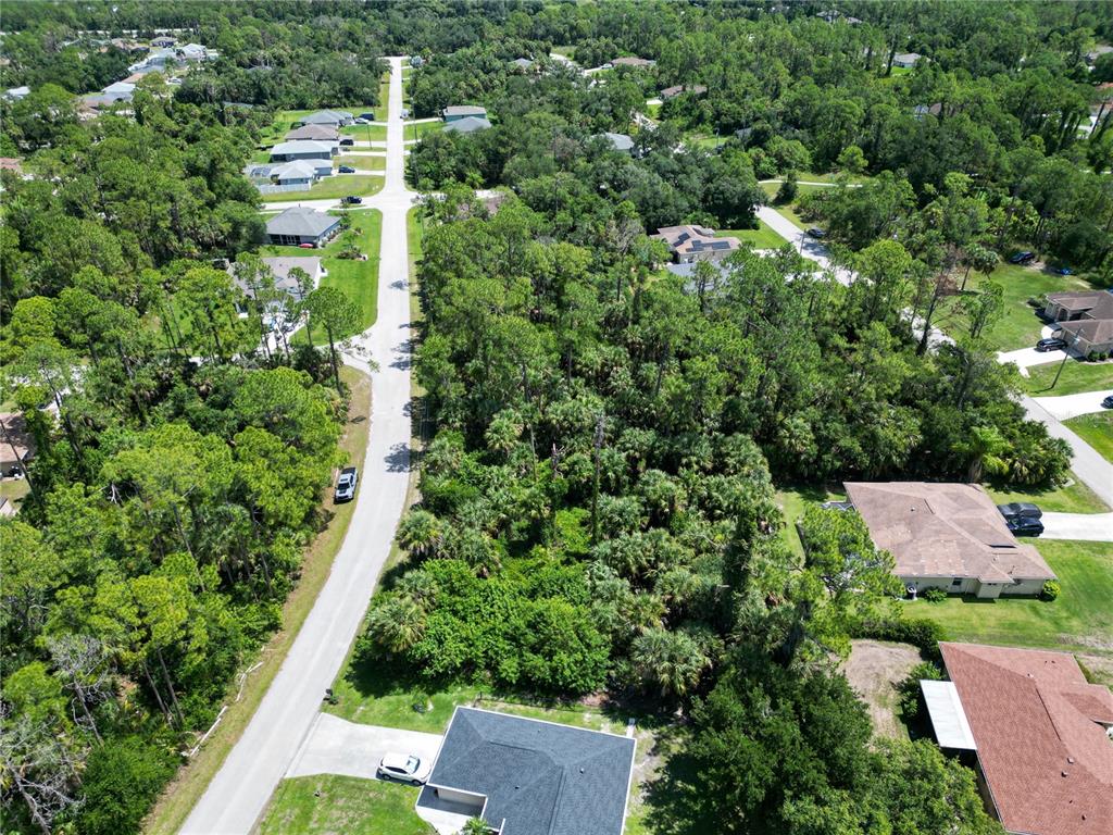 An aerial view shows a residential street lined with houses surrounded by dense green trees — MAYWOOD LANE, NORTH PORT, FL