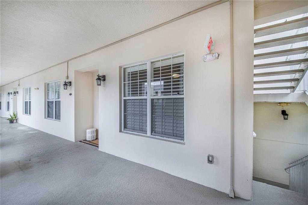 An exterior walkway features a white wall with windows, an exit sign, and a staircase — 2315 UPPER PARK ROAD UNIT 9-203, ORLANDO, FL