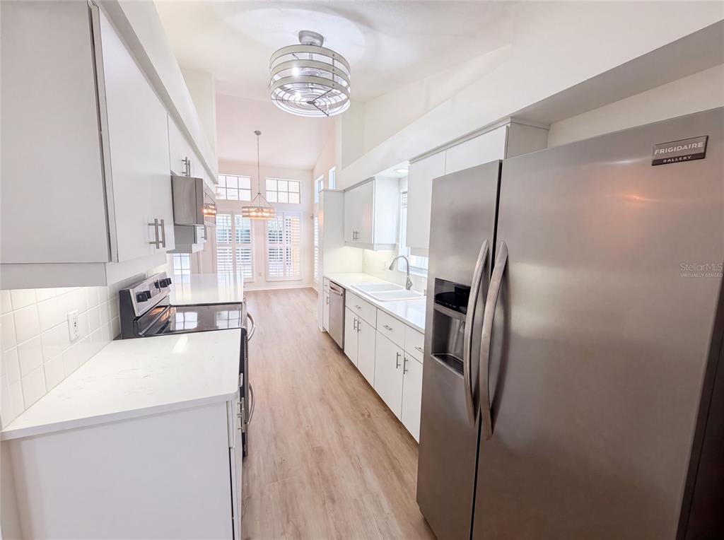 A galley kitchen features white cabinets, stainless steel appliances, and light wood-look flooring — 9454 MISSISSIPPI RUN, WEEKI WACHEE, FL