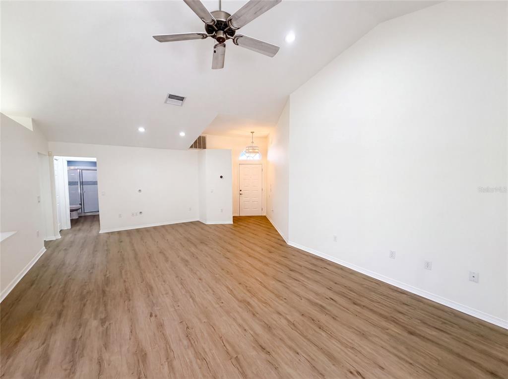 A spacious living room features vaulted ceilings, a ceiling fan, and light-colored wood-look flooring — 9454 MISSISSIPPI RUN, WEEKI WACHEE, FL