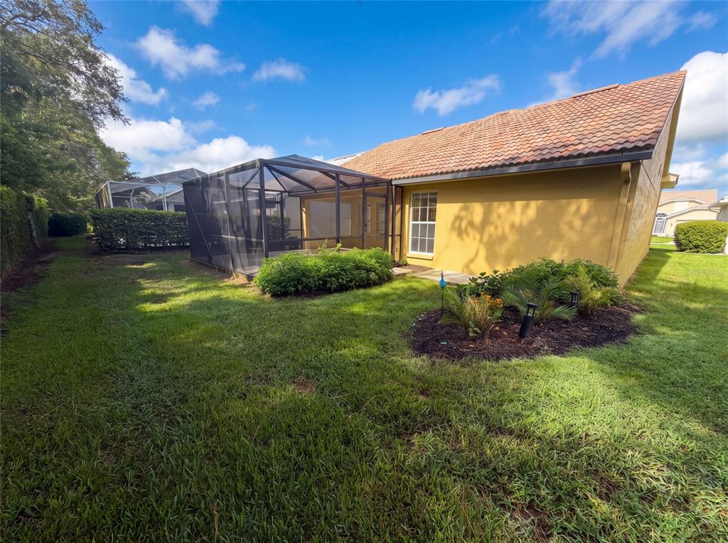 A yellow house with a tiled roof and a screened-in patio overlooks a grassy backyard — 9454 MISSISSIPPI RUN, WEEKI WACHEE, FL