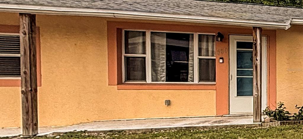 The exterior of a house features a tan stucco wall, a front door, and windows — 880 EMERALD DR, MOUNT DORA, FL