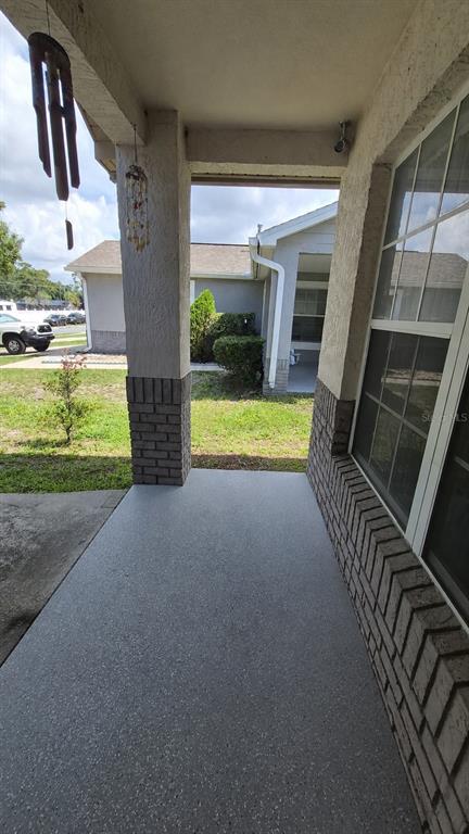 A covered concrete porch features a brick-accented pillar and a view of the yard — 121 S ROMA WAY, KISSIMMEE, FL