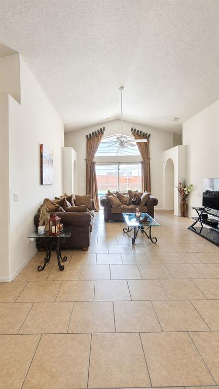 A living room with tile floors, a vaulted ceiling, and a view of a pool — 121 S ROMA WAY, KISSIMMEE, FL