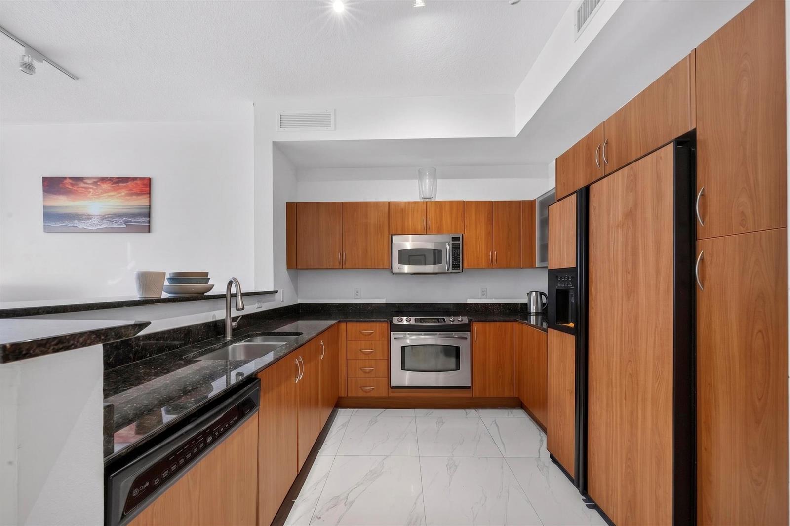A modern kitchen features wood cabinets, stainless steel appliances, dark countertops, and white marble flooring — 804 E Windward Way # 111, Lantana FL 33462, LANTANA, FL