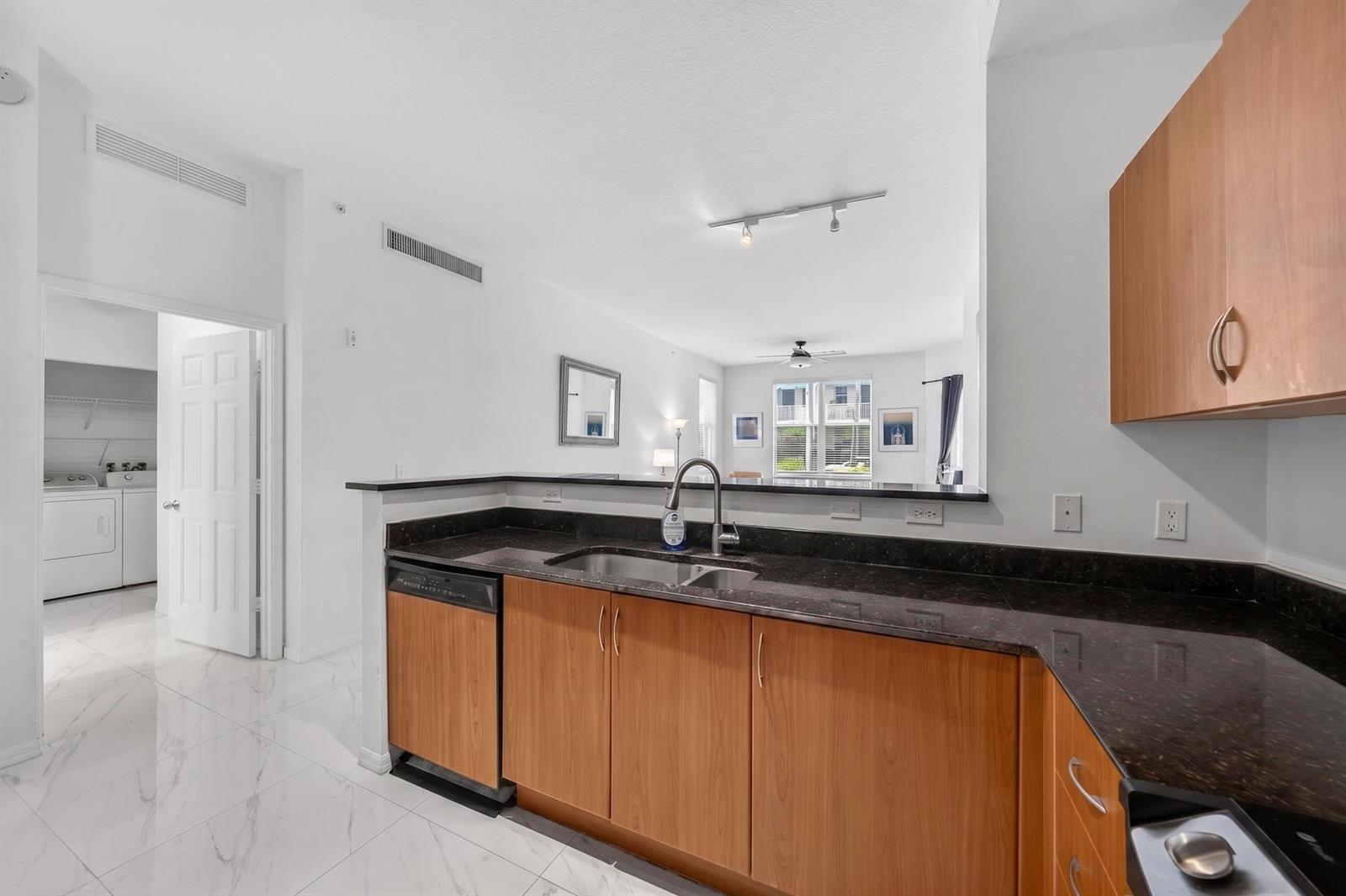 A kitchen with wood cabinets, dark granite countertops, and white tile flooring overlooks a living area — 804 E Windward Way # 111, Lantana FL 33462, LANTANA, FL