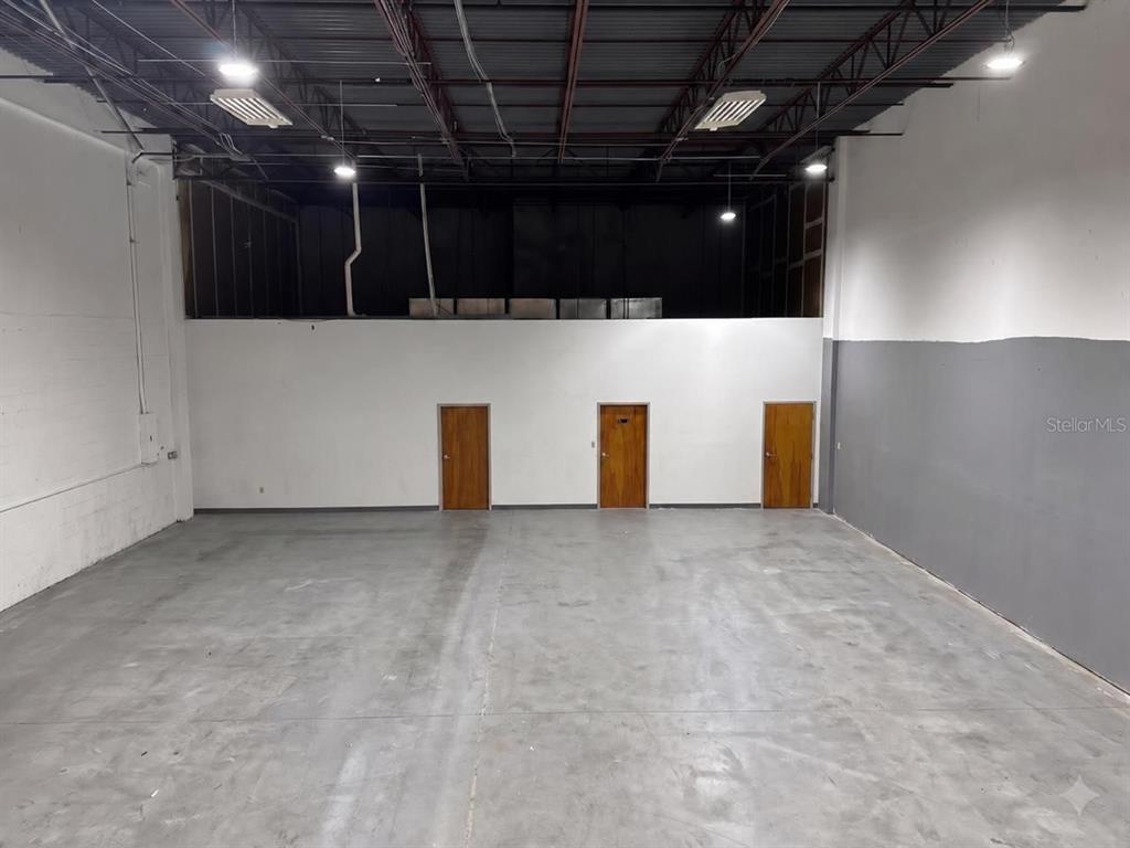 An empty industrial warehouse space features a concrete floor, three wooden doors, and exposed ceiling — 9777 SATELLITE BOULEVARD, ORLANDO, FL