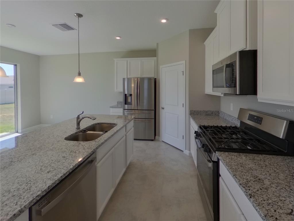A kitchen features white cabinets, granite countertops, stainless steel appliances, and a central island — 11611 GOLD DUST COURT, RIVERVIEW, FL