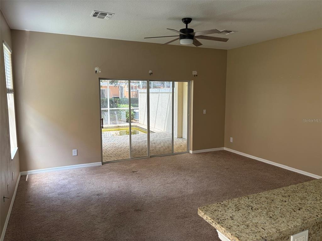 A carpeted living room features a ceiling fan, sliding glass doors, and a view of a pool — 1407 RETREAT CIRCLE, CLERMONT, FL