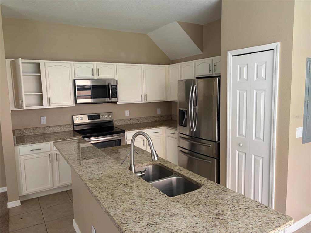 A kitchen features white cabinets, granite countertops, stainless steel appliances, and a central island sink — 1407 RETREAT CIRCLE, CLERMONT, FL