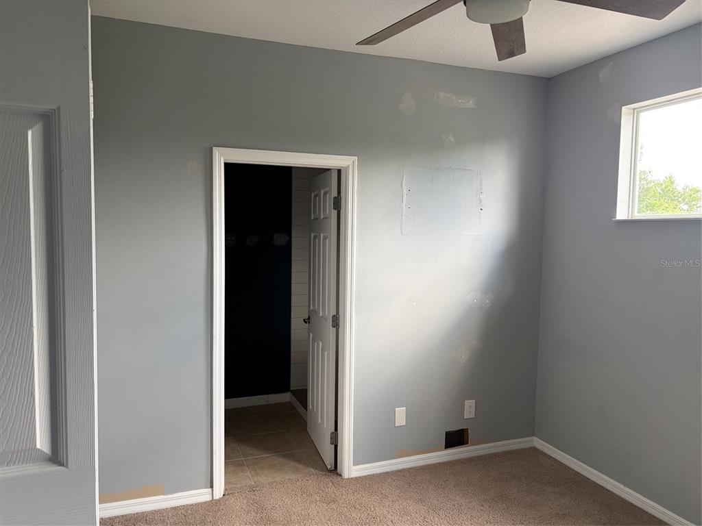 A bedroom with gray walls, beige carpeting, and an open doorway leading to a bathroom — 1407 RETREAT CIRCLE, CLERMONT, FL