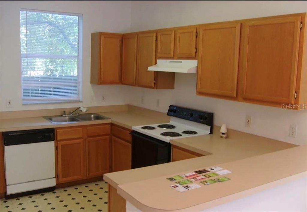 A kitchen features wood cabinets, laminate countertops, a white dishwasher, and a white electric stove — 4415 SW 34TH STREET UNIT 708, GAINESVILLE, FL