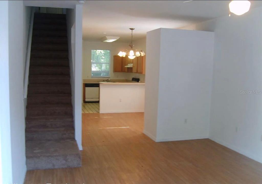 A view of a living area with stairs, wood-look flooring, and an open kitchen beyond — 4415 SW 34TH STREET UNIT 708, GAINESVILLE, FL