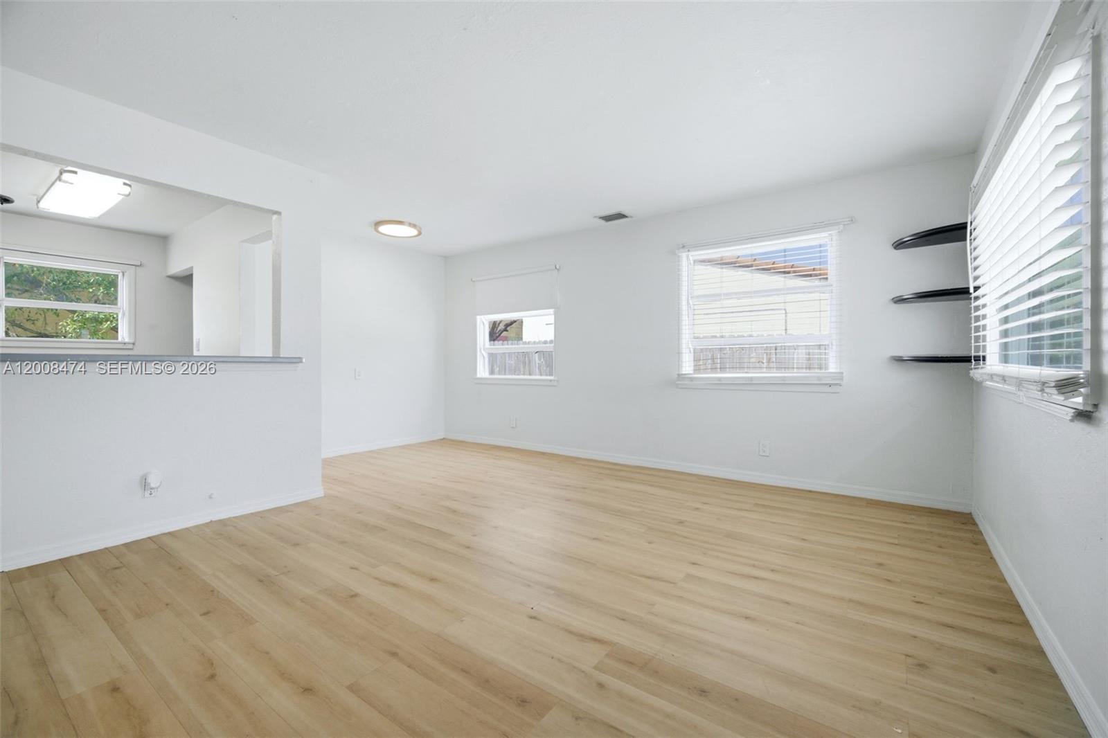 An empty room features light wood-look flooring, white walls, multiple windows, and black wall shelves — 2124 Taylor St, Hollywood FL 33020, HOLLYWOOD, FL