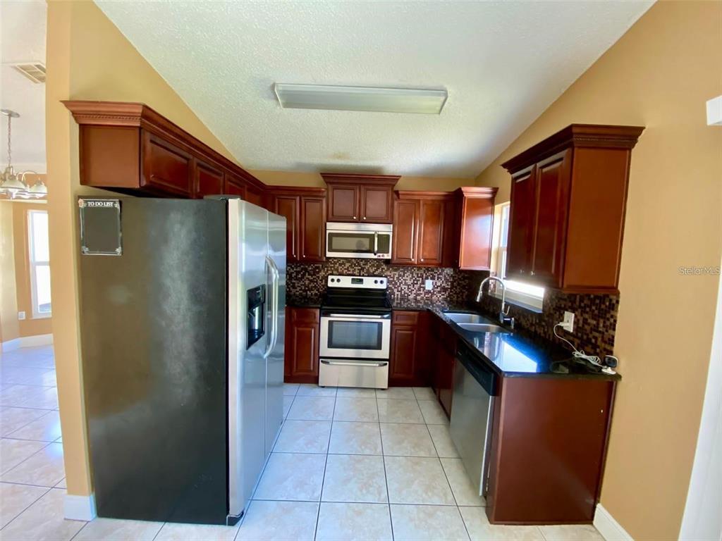 A kitchen features dark wood cabinets, stainless steel appliances, black countertops, and light tile flooring — 880 NELSON DRIVE, KISSIMMEE, FL