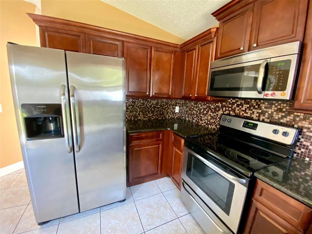 A kitchen features dark wood cabinets, stainless steel appliances, and a mosaic tile backsplash — 880 NELSON DRIVE, KISSIMMEE, FL