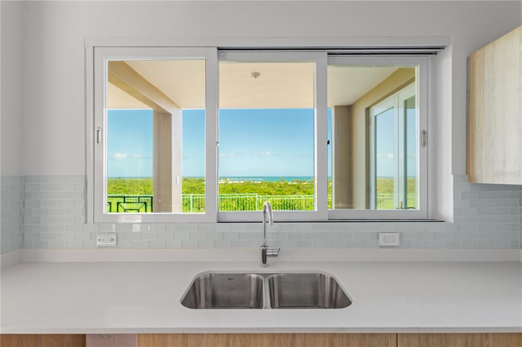 A kitchen sink sits below a large window overlooking a balcony and the ocean — 10 I UNIT 201, RIO GRANDE, PR