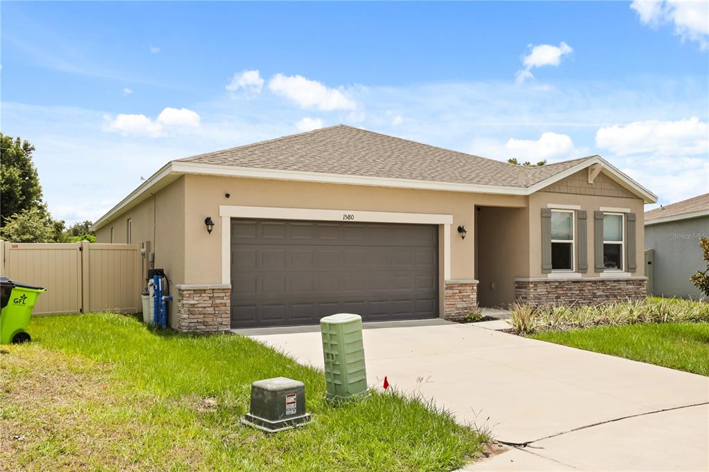 A single-story suburban house with a tan stucco exterior, stone accents, and a two-car garage — 1580 BLUE LAGOON CIRCLE, MASCOTTE, FL