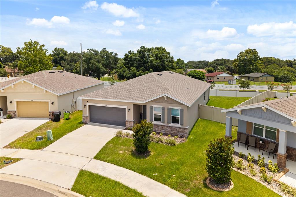 An aerial view shows three suburban houses with driveways and lawns under a blue sky — 1580 BLUE LAGOON CIRCLE, MASCOTTE, FL