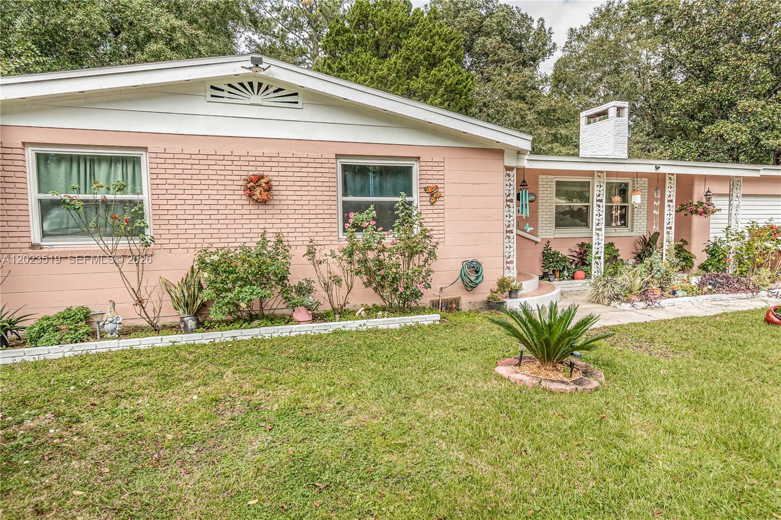 A single-story pink brick house features a white chimney, decorative porch columns, and landscaping — 145 N ORANGE ST, Starke FL 32091, STARKE, FL