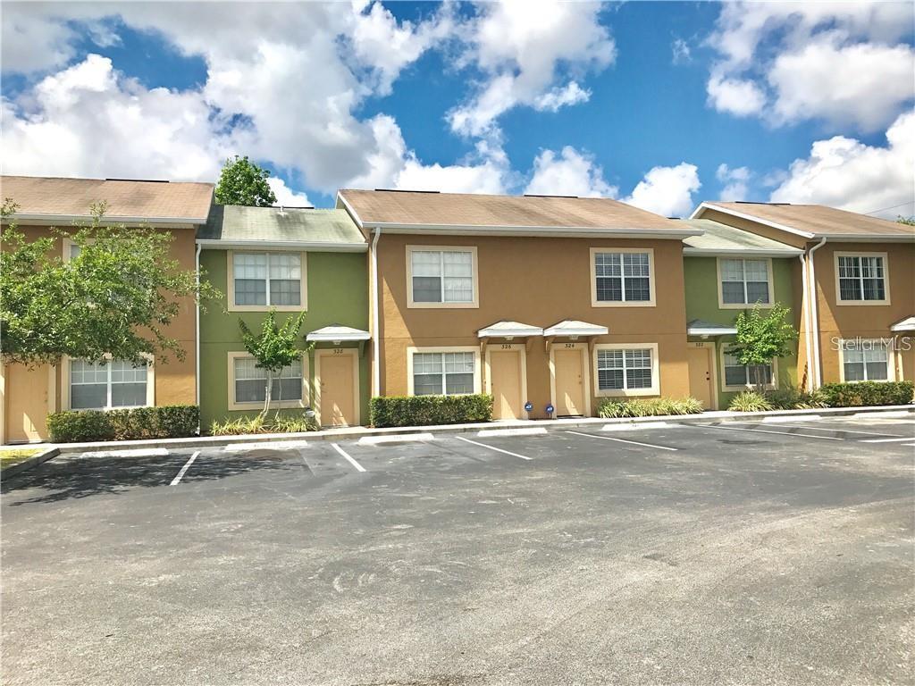 A row of multi-story townhouses with tan and green siding faces a paved parking lot — 354 CERVANTES DRIVE, KISSIMMEE, FL