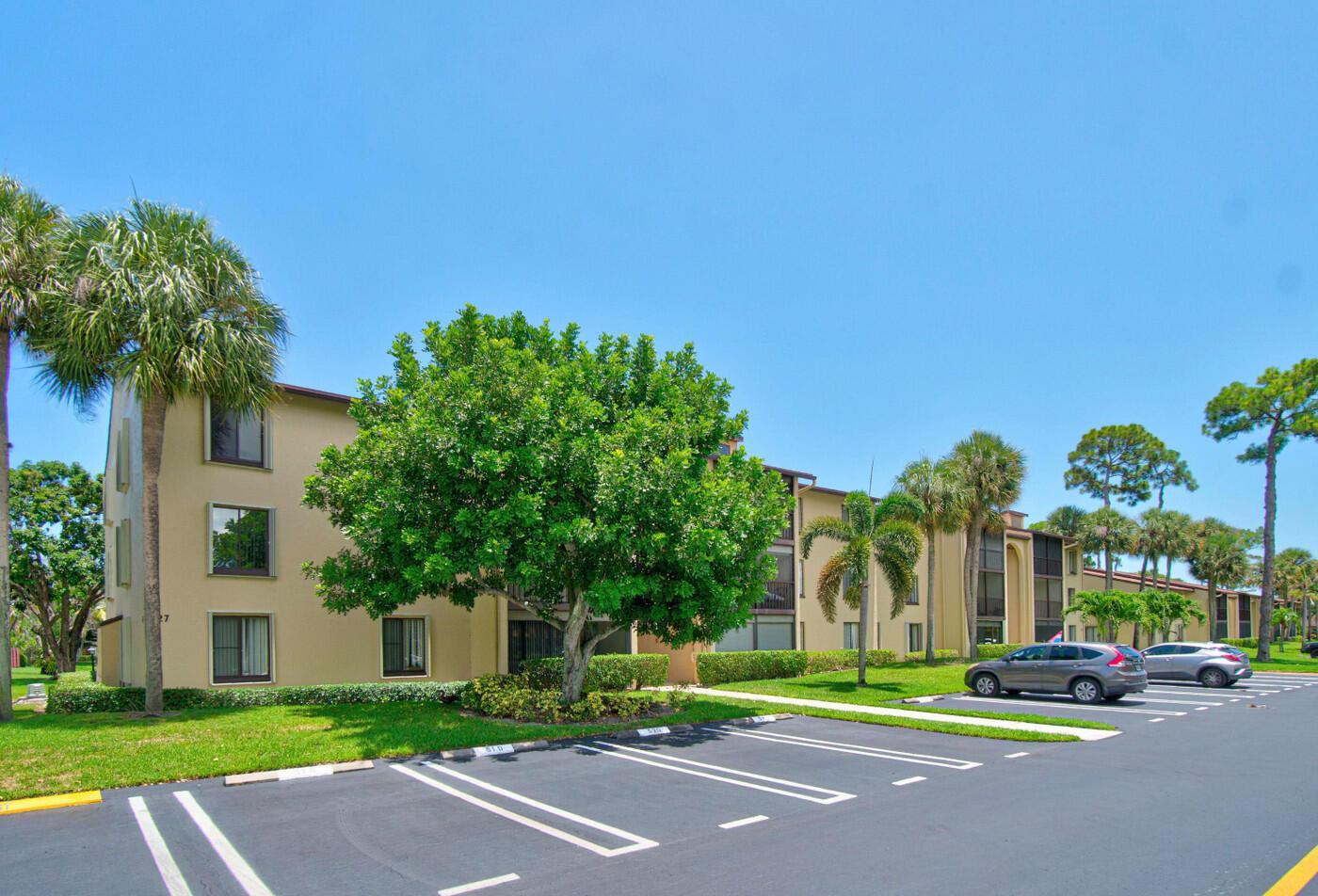 A multi-story apartment building with a parking lot and palm trees under a clear sky — 627 Sea Pine Way # A3, FL 33415, FL