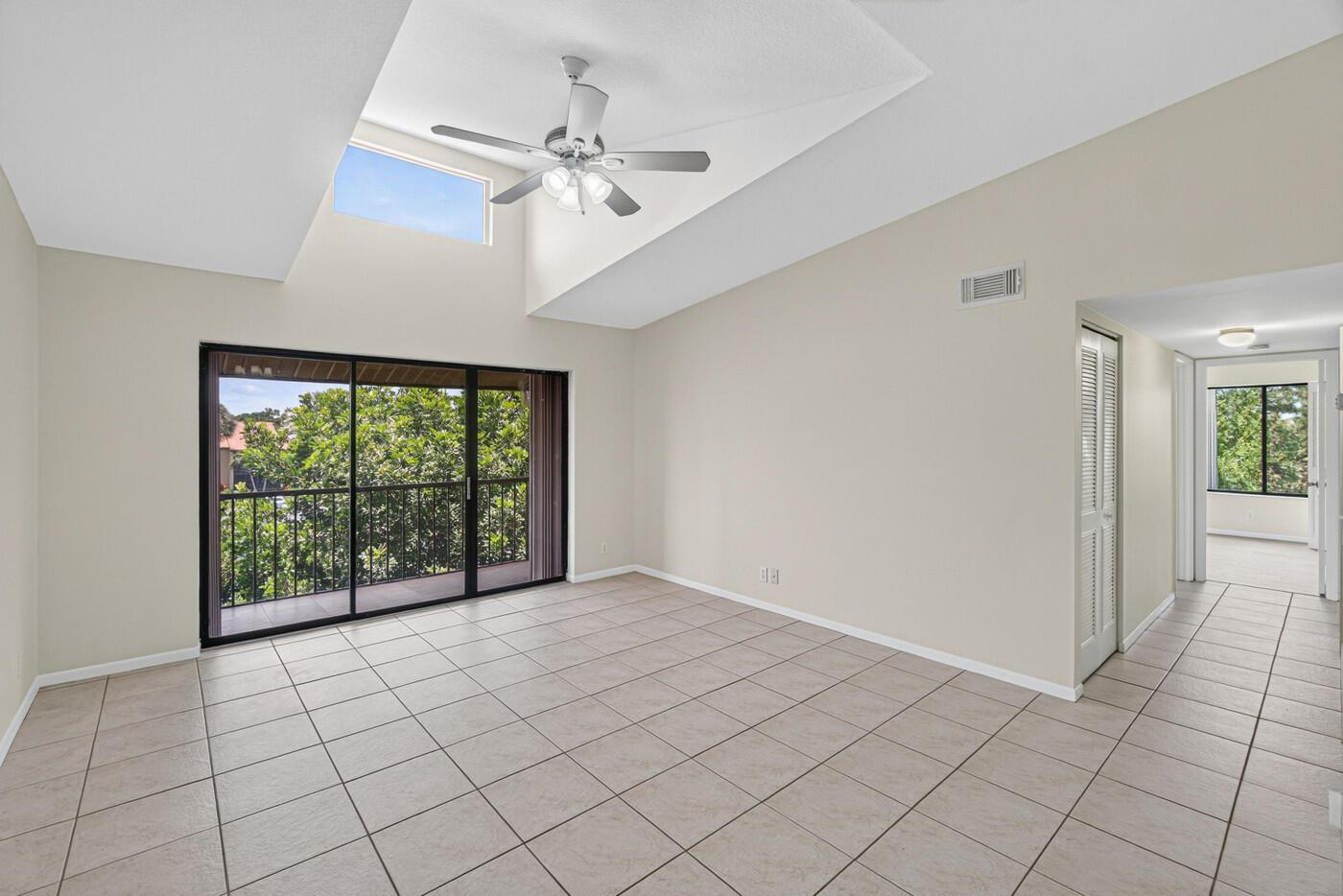 An empty room with beige tile flooring, a vaulted ceiling, and a sliding glass door — 627 Sea Pine Way # A3, FL 33415, FL
