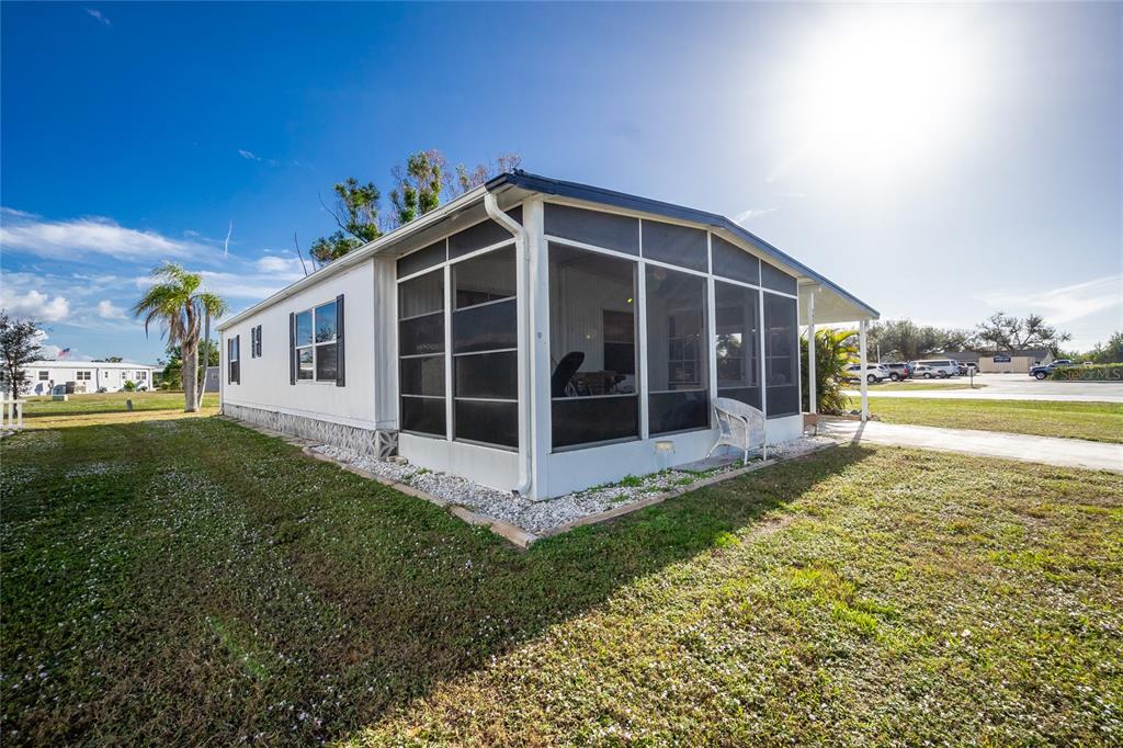 A white mobile home features a large screened-in porch and a gravel border on grass — 7474 FULMAR AVENUE, PORT CHARLOTTE, FL