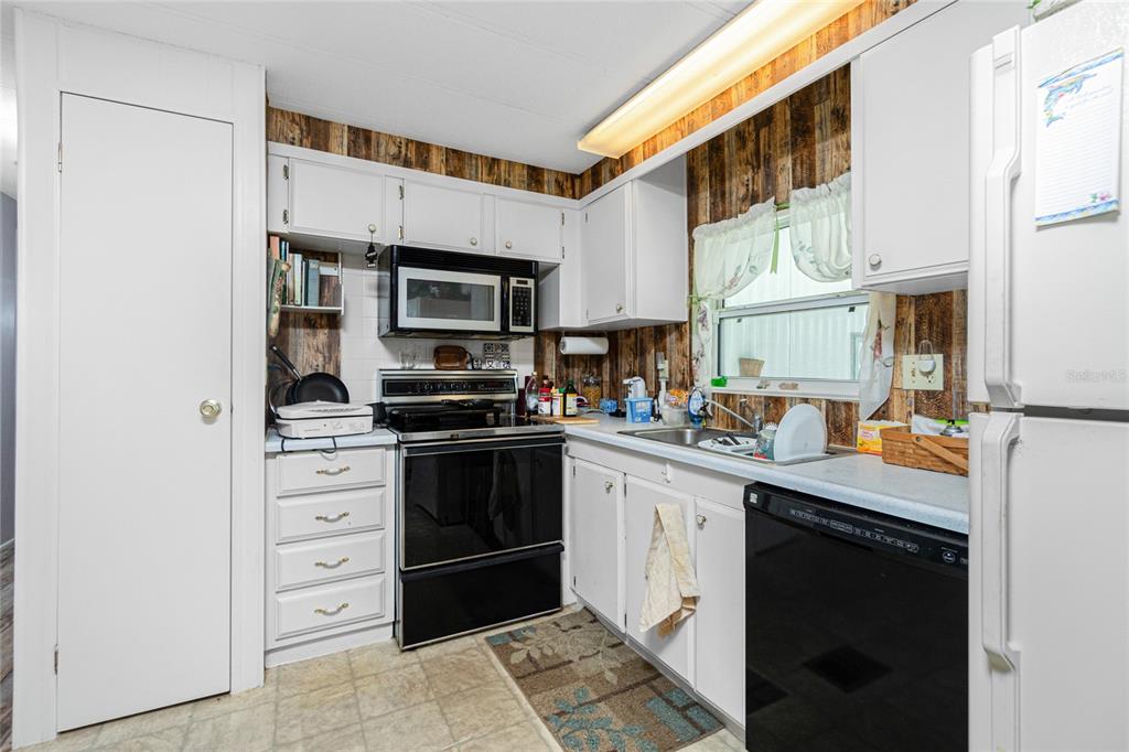 A kitchen features white cabinets, wood-paneled walls, black appliances, and a window above the sink — 7474 FULMAR AVENUE, PORT CHARLOTTE, FL