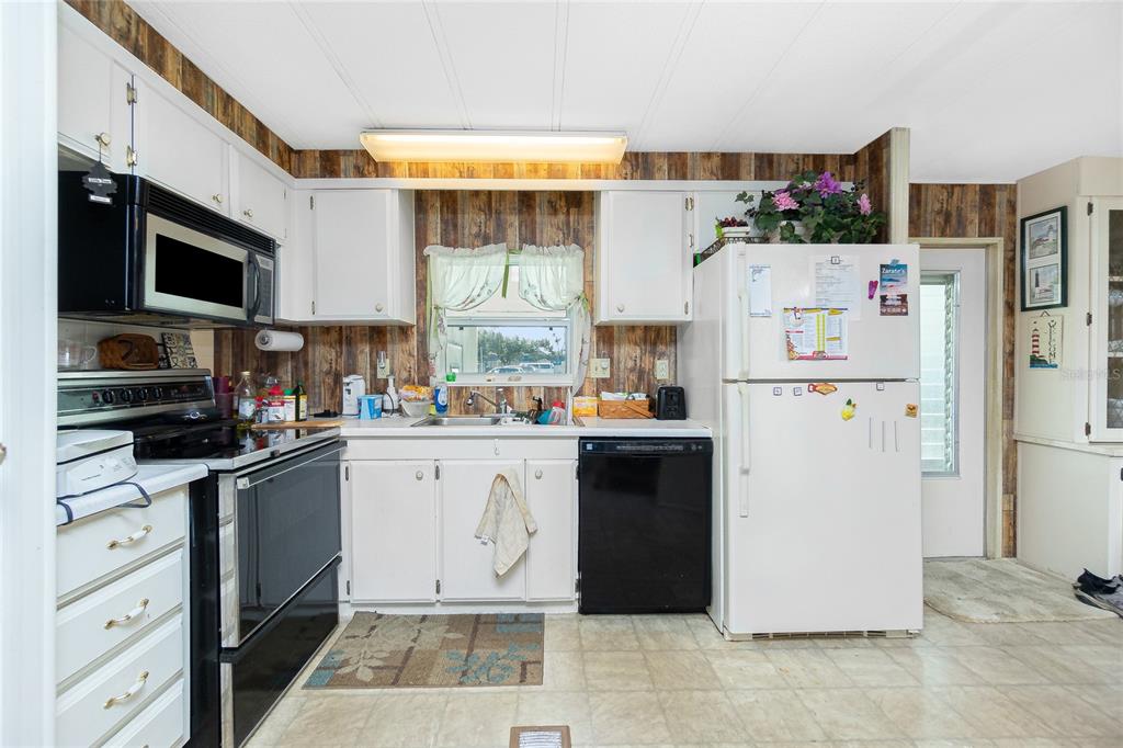 A kitchen with white cabinets, wood-paneled walls, a black dishwasher, and a white refrigerator — 7474 FULMAR AVENUE, PORT CHARLOTTE, FL