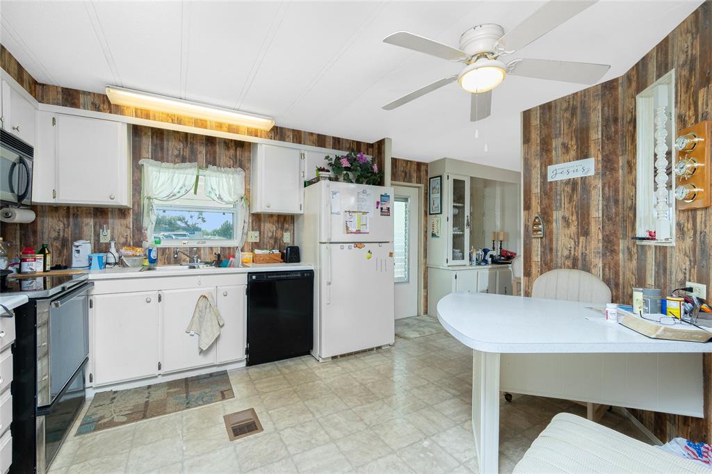 A kitchen features white cabinets, wood-paneled walls, a white dining table, and a ceiling fan — 7474 FULMAR AVENUE, PORT CHARLOTTE, FL