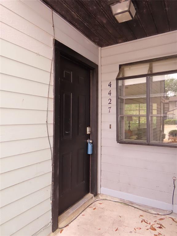 A black front door with a lockbox is located next to a window on a porch — 4427 SW 21ST LANE, GAINESVILLE, FL
